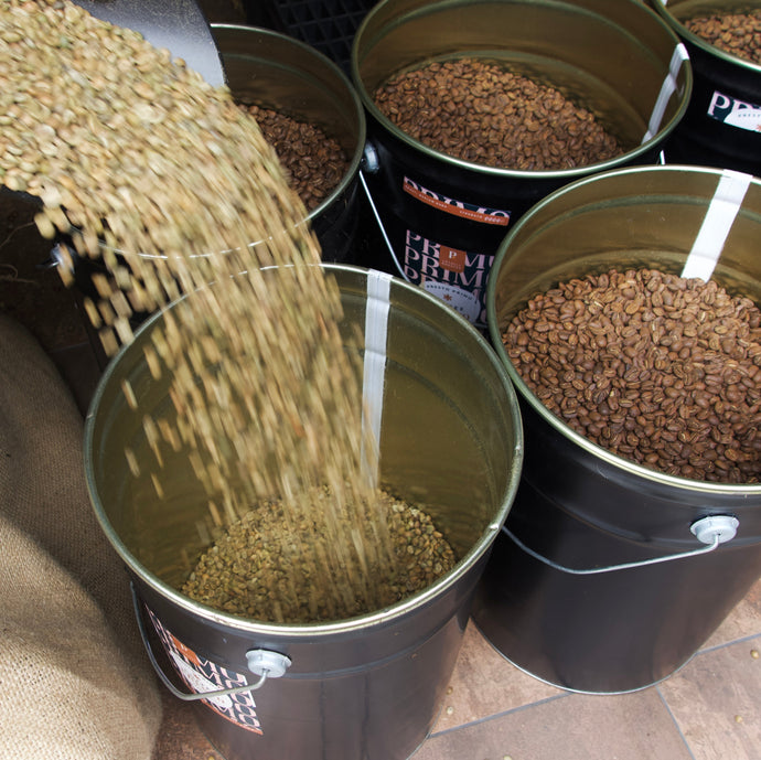 coffee beans being poured into a black bucket with other similar buckets in the background.